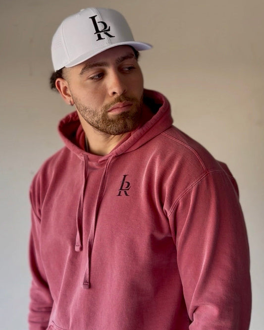 Man wearing a white cap and red hoodie with a logo, standing in a garage.