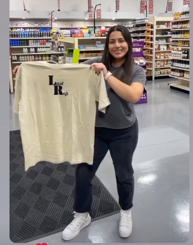 Person holding a beige Last Rep t-shirt  in a store setting