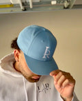 Person wearing a light blue cap with a logo, holding it up to their face.