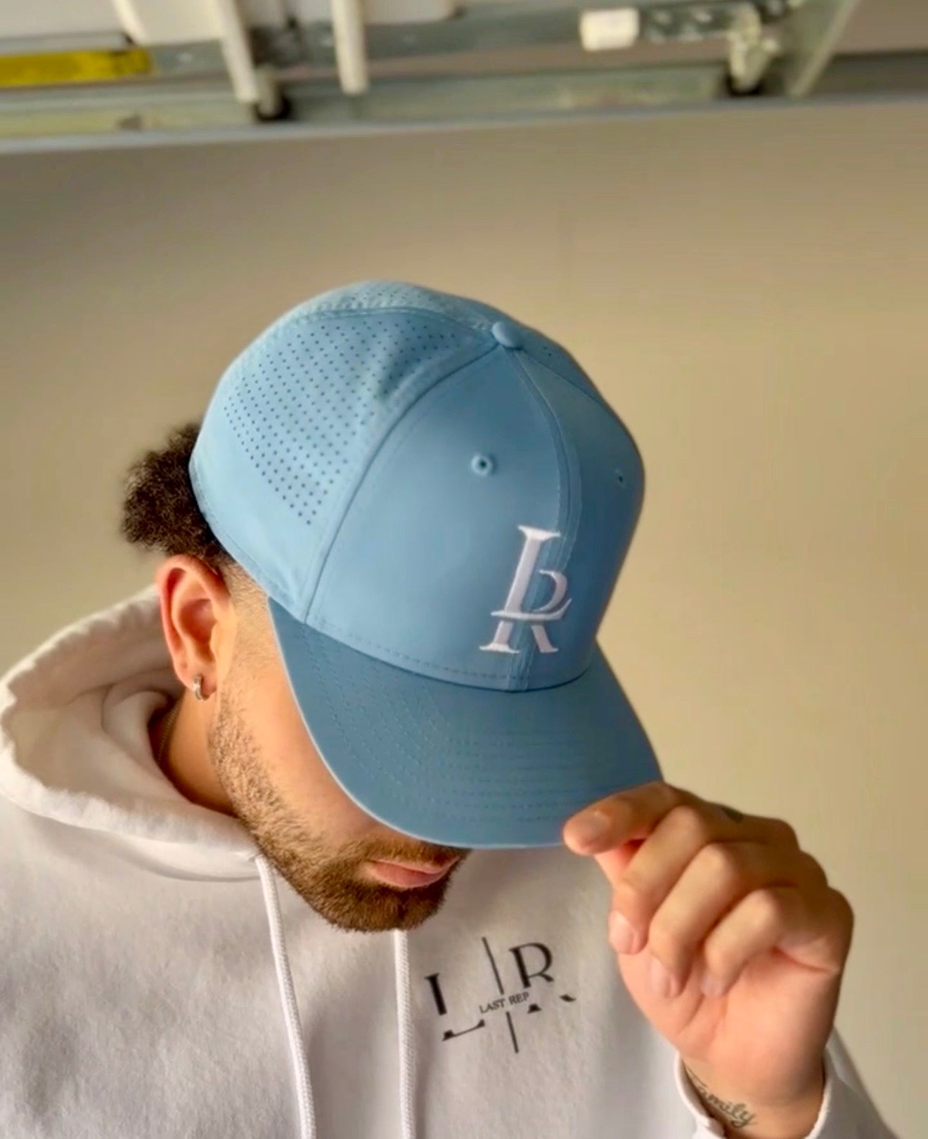 Person wearing a light blue cap with a logo, holding it up to their face.