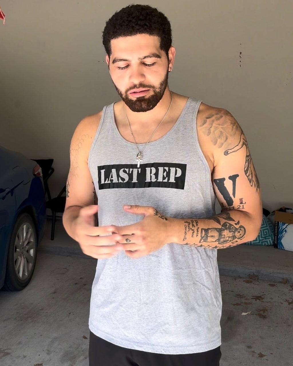 Man wearing a 'Last Rep' tank top in a garage.