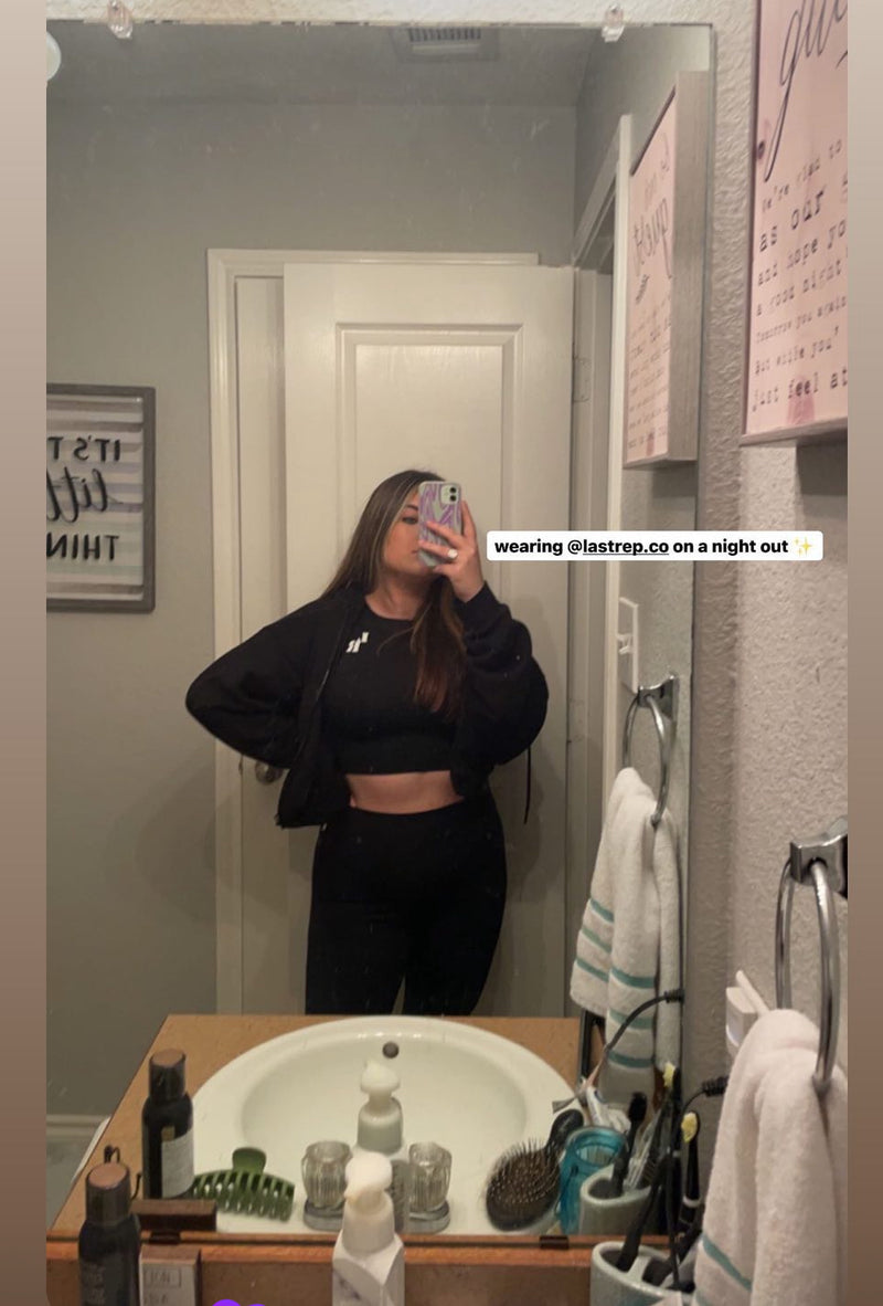 Person taking a mirror selfie in a bathroom wearing a black Last Rep outfit.