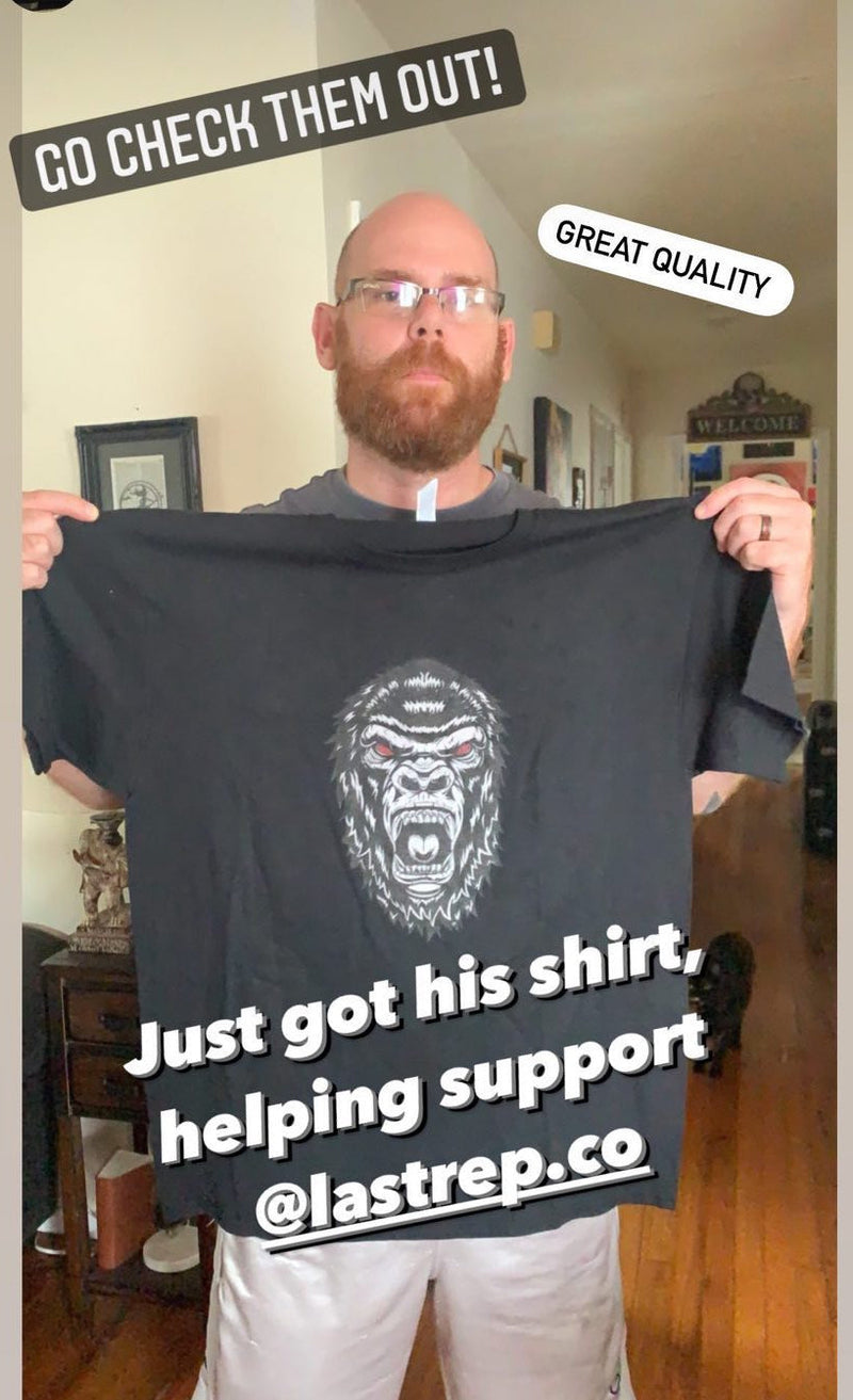 Man holding a black Last Rep t-shirt with a graphic design, standing in a room.