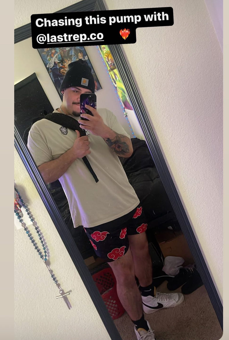 Person taking a mirror selfie wearing a tan Last Rep t-shirt and black shorts with red patterns, holding a phone.