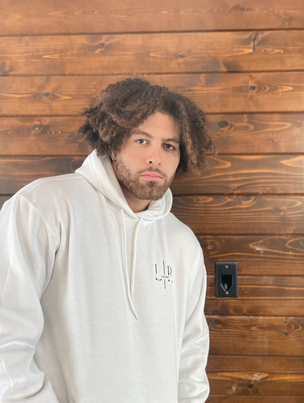 A person wearing a white hoodie with text on it standing in front of a wooden background.