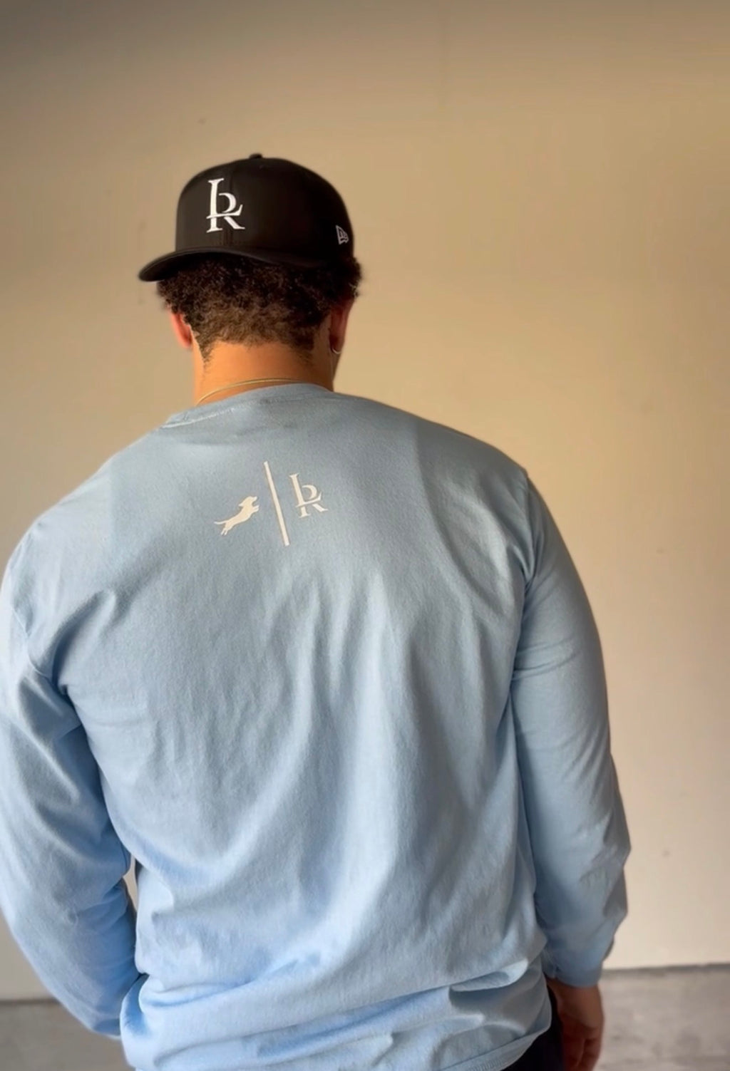 Person wearing a light blue long-sleeve shirt with a logo on the back, standing against a plain background.