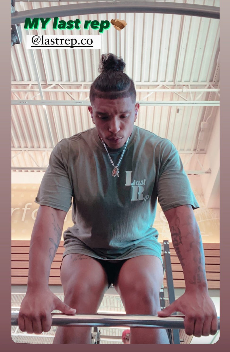 Person exercising with a barbell in a gym setting, wearing a 'Last Rep' t-shirt.