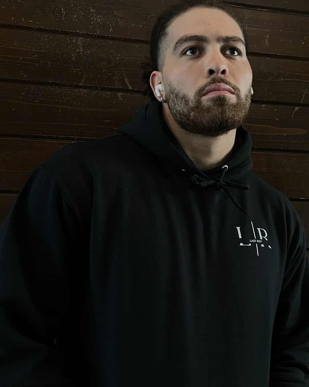 Man wearing a black hoodie with a Last Rep logo against a wooden wall