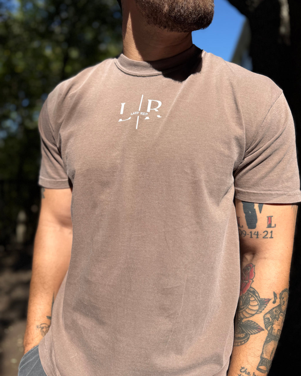 Man wearing a brown t-shirt with a logo outdoors