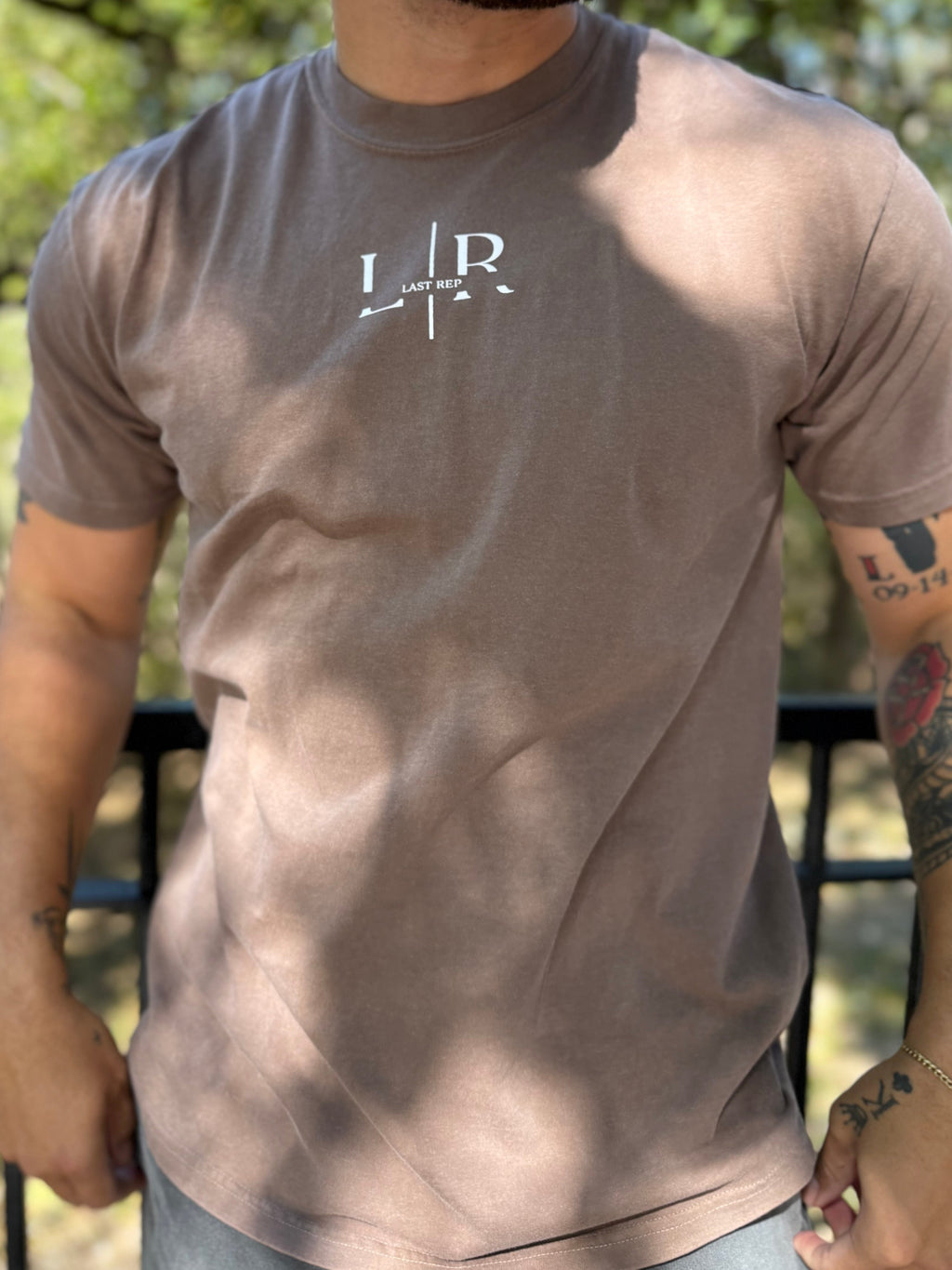Man wearing a brown t-shirt with a logo outdoors