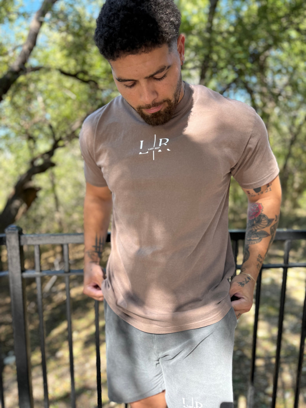 Man wearing a beige t-shirt with a logo outdoors