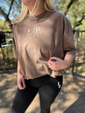 Person wearing a brown oversized t-shirt with a logo and black leggings outdoors.