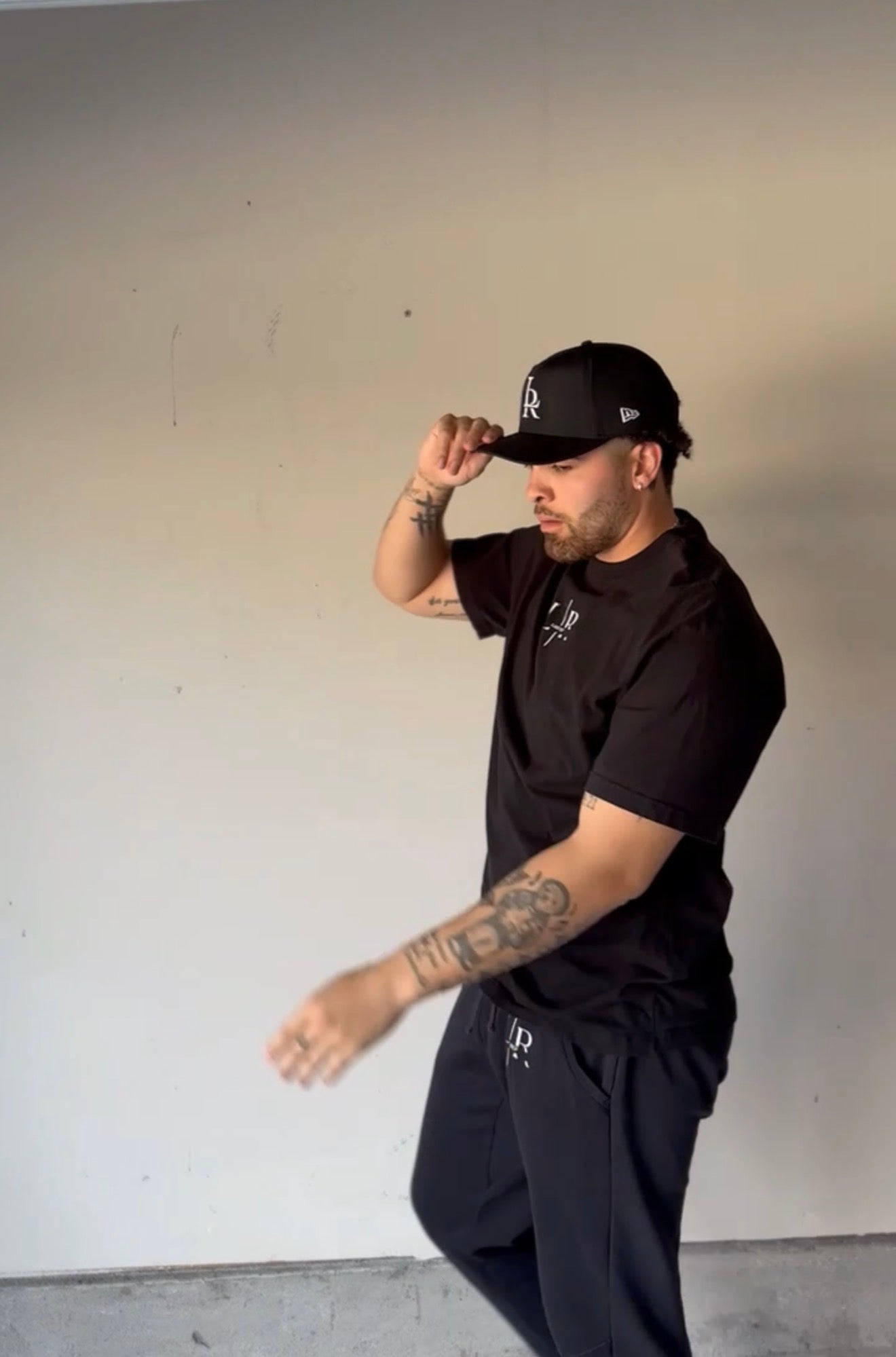 Man wearing a black cap and black shirt against a plain wall