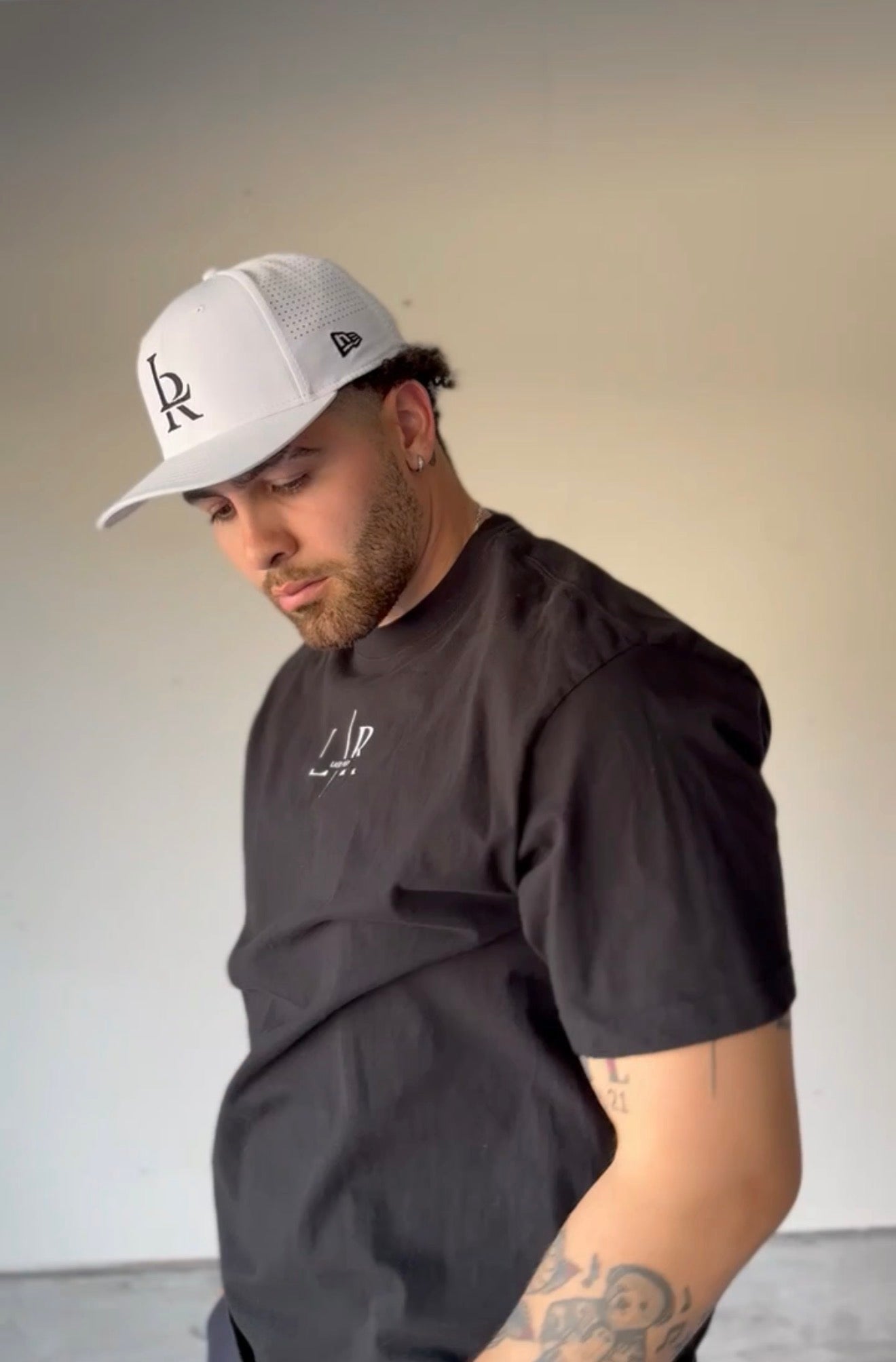 Man wearing a black t-shirt and white cap with a logo, standing against a plain background