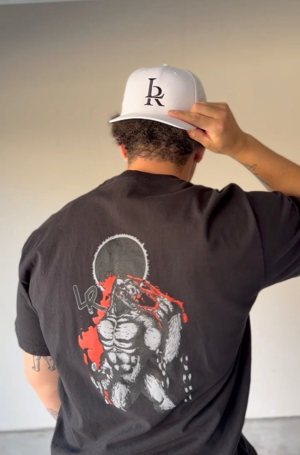 Person wearing a black t-shirt with a graphic design and a white cap with a logo.