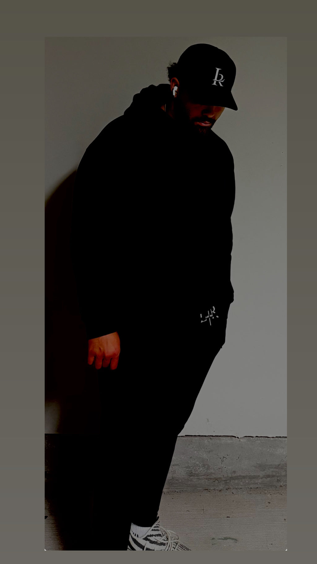 Person wearing a black hoodie and cap against a plain wall