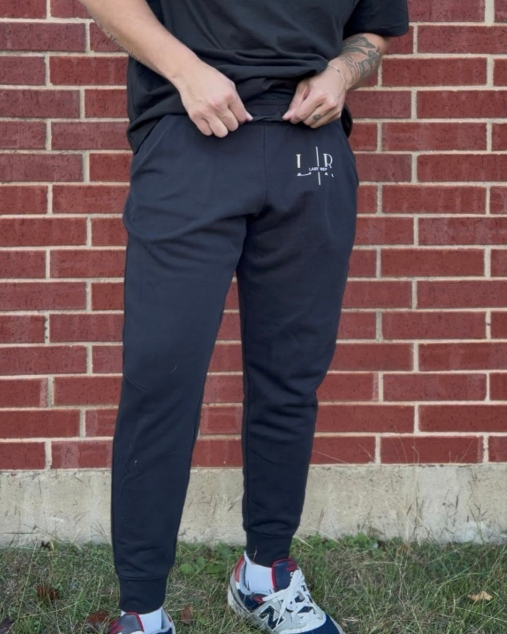 Person wearing navy jogger pants with a logo against a brick wall.