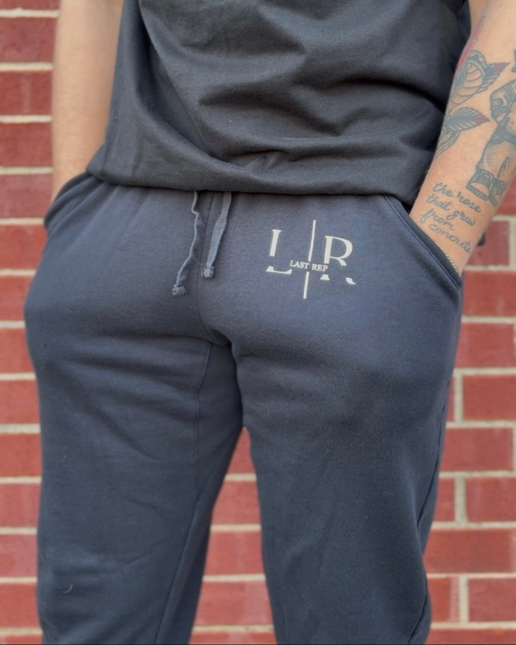 Person wearing navy blue jogger pants with a logo against a brick wall