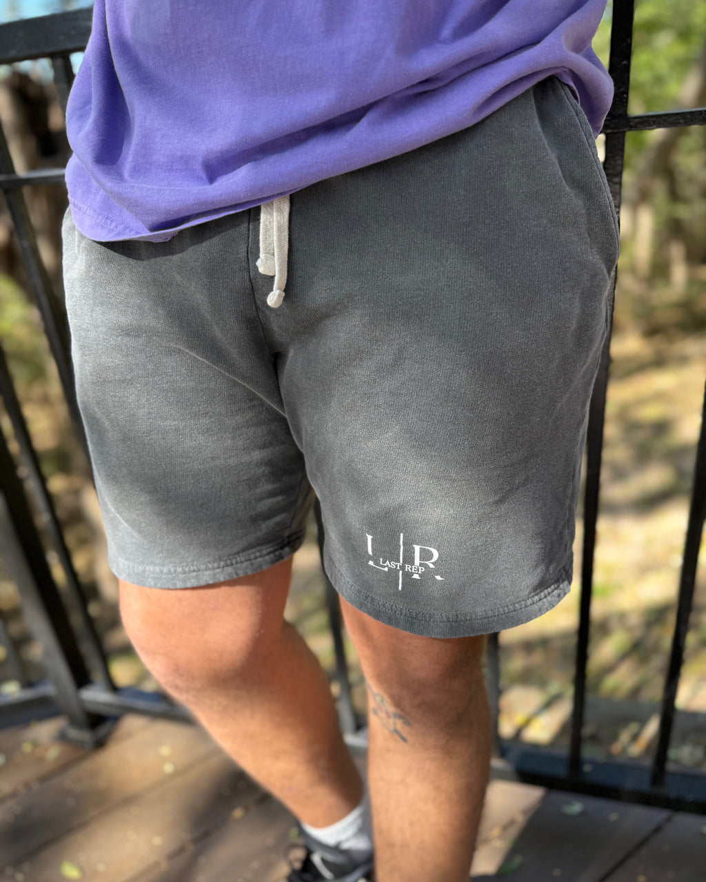 Person wearing gray shorts with a logo on a blurred outdoor background