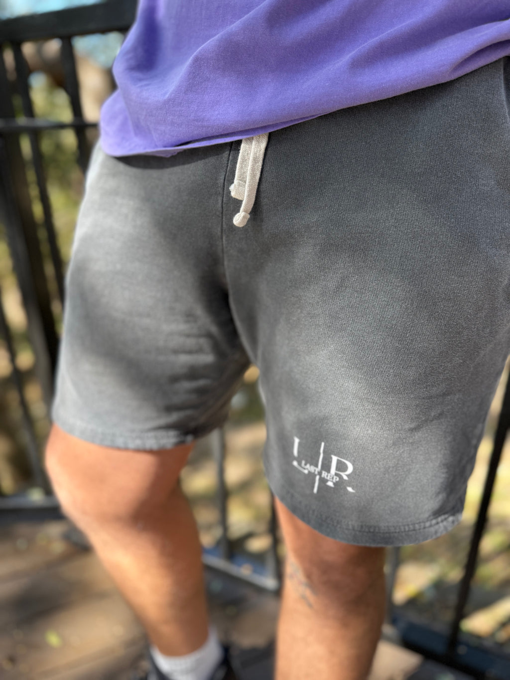 Person wearing gray shorts with a logo and purple top, standing outdoors.