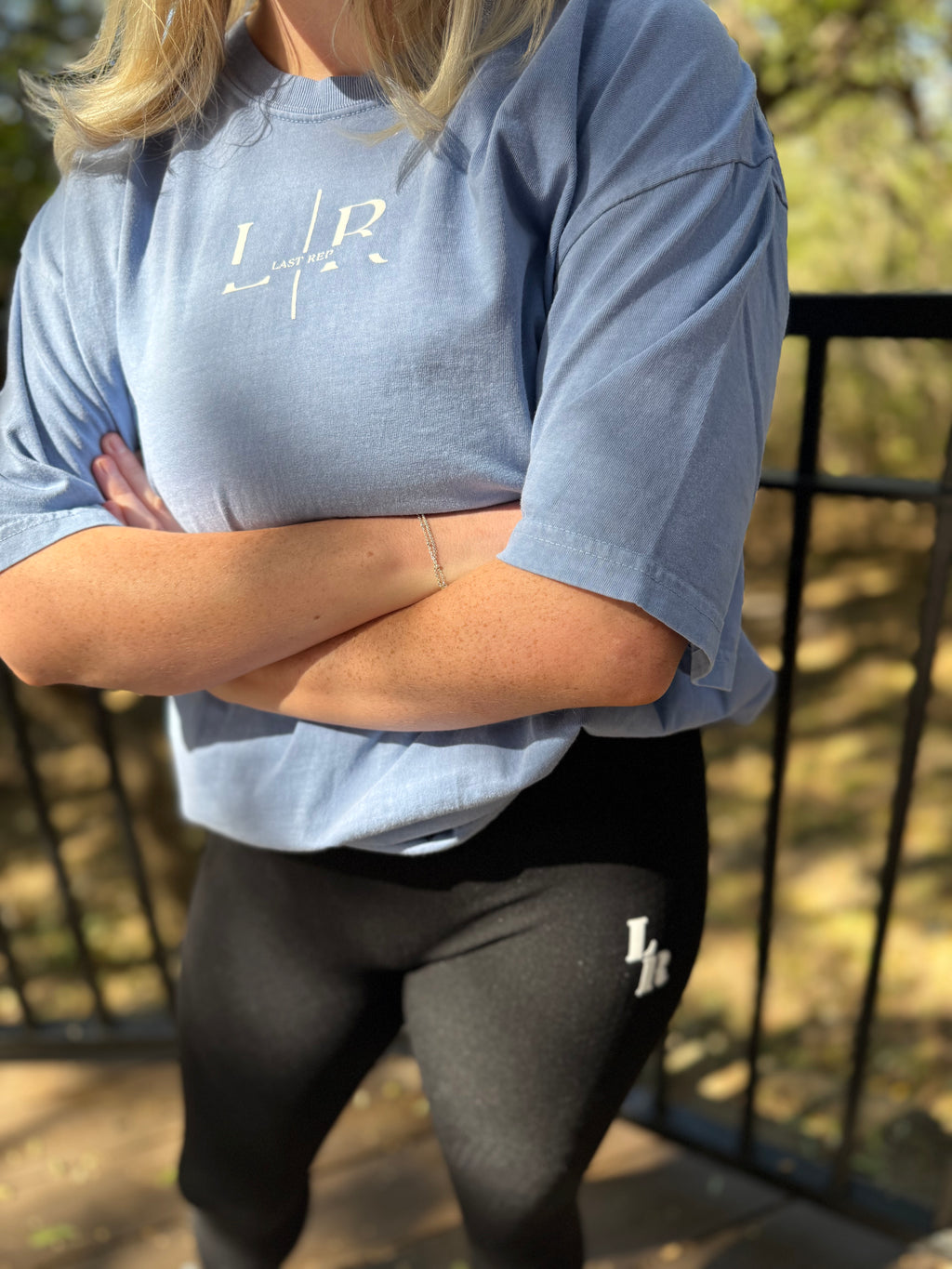 Person wearing a blue shirt and black leggings with a logo, standing outdoors.