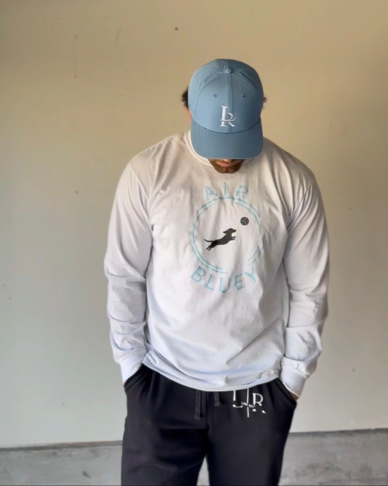 Person wearing a white long sleeve shirt with a logo and text, paired with a blue cap indoors.