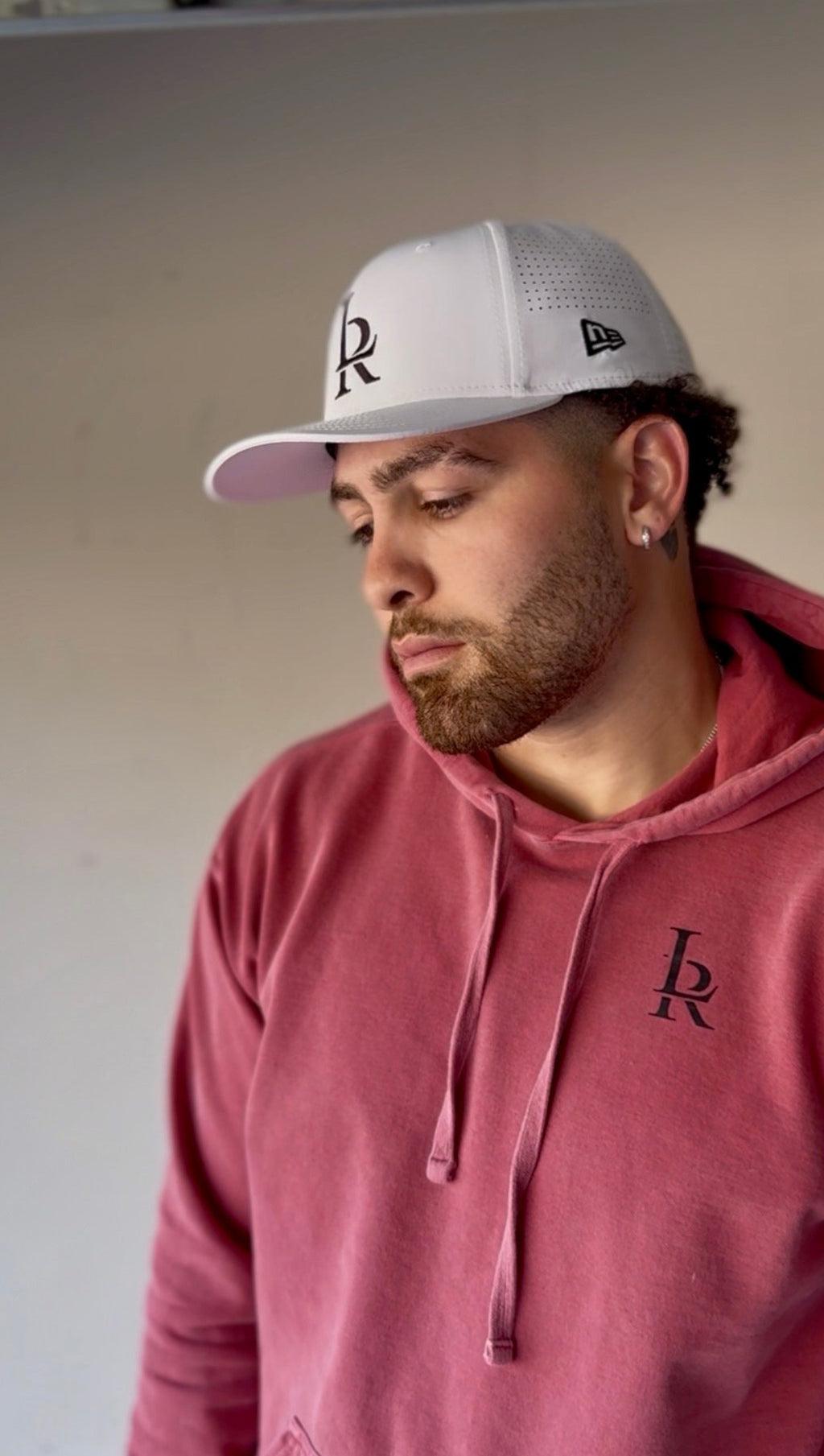 Man wearing a red hoodie and gray cap with a logo, standing in an indoor setting