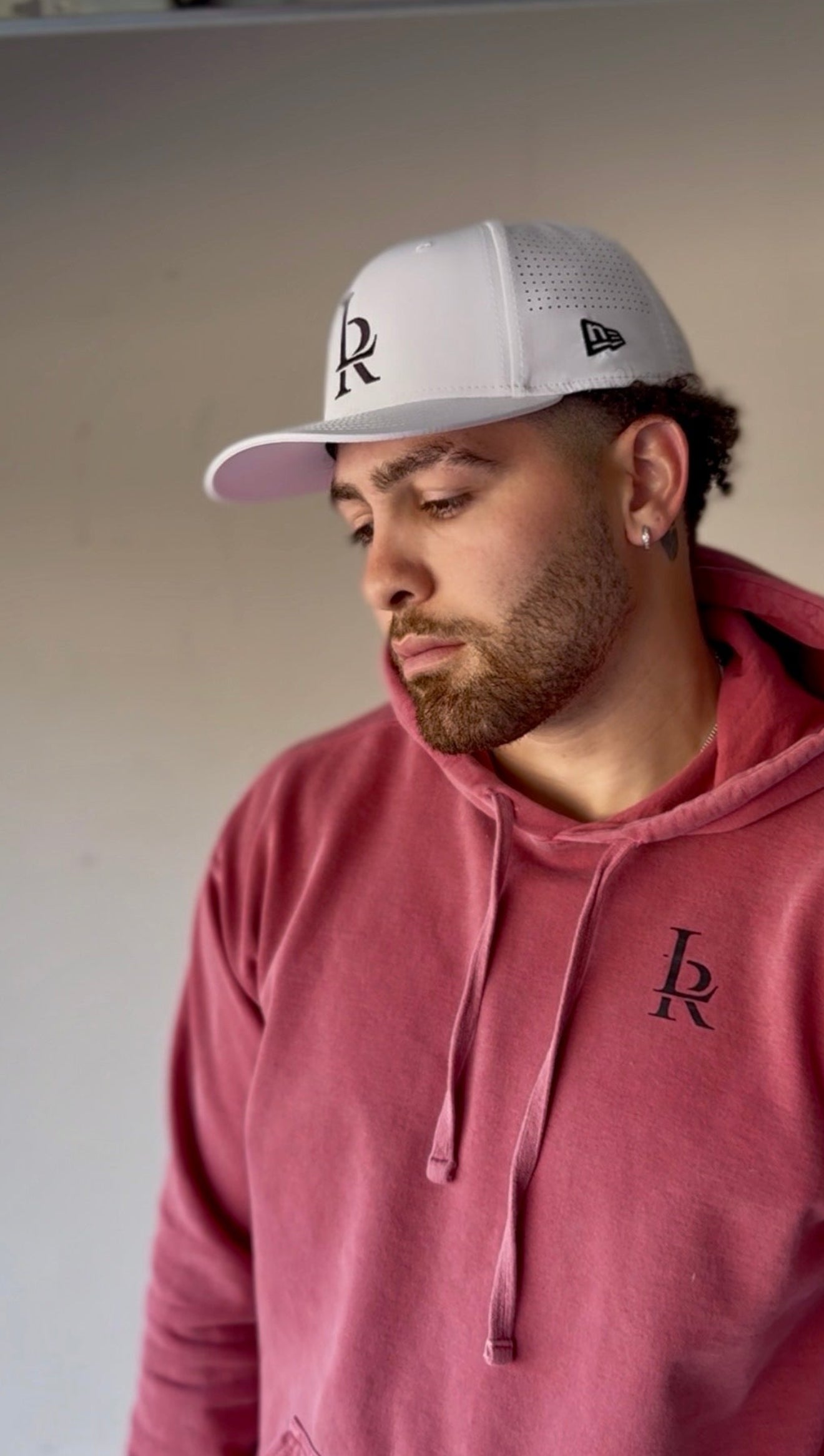 Man wearing a red hoodie and gray cap with a logo, standing in an indoor setting