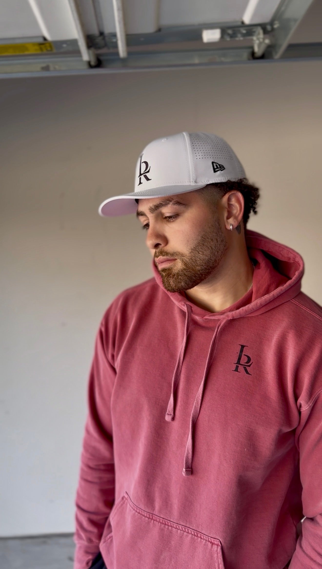 Man wearing a red hoodie and gray cap with a logo, standing in an indoor setting