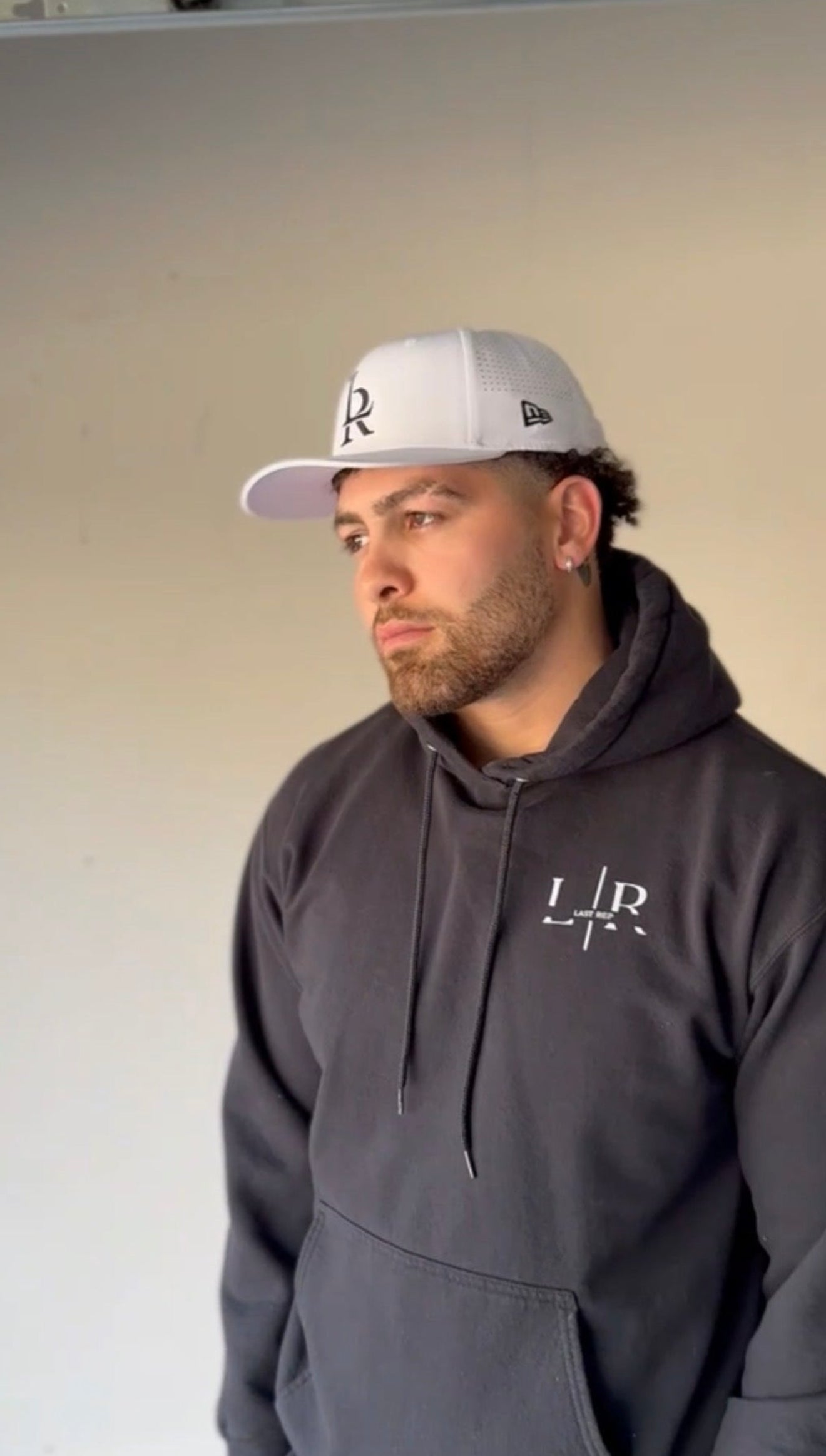 Man wearing a dark hoodie and cap indoors