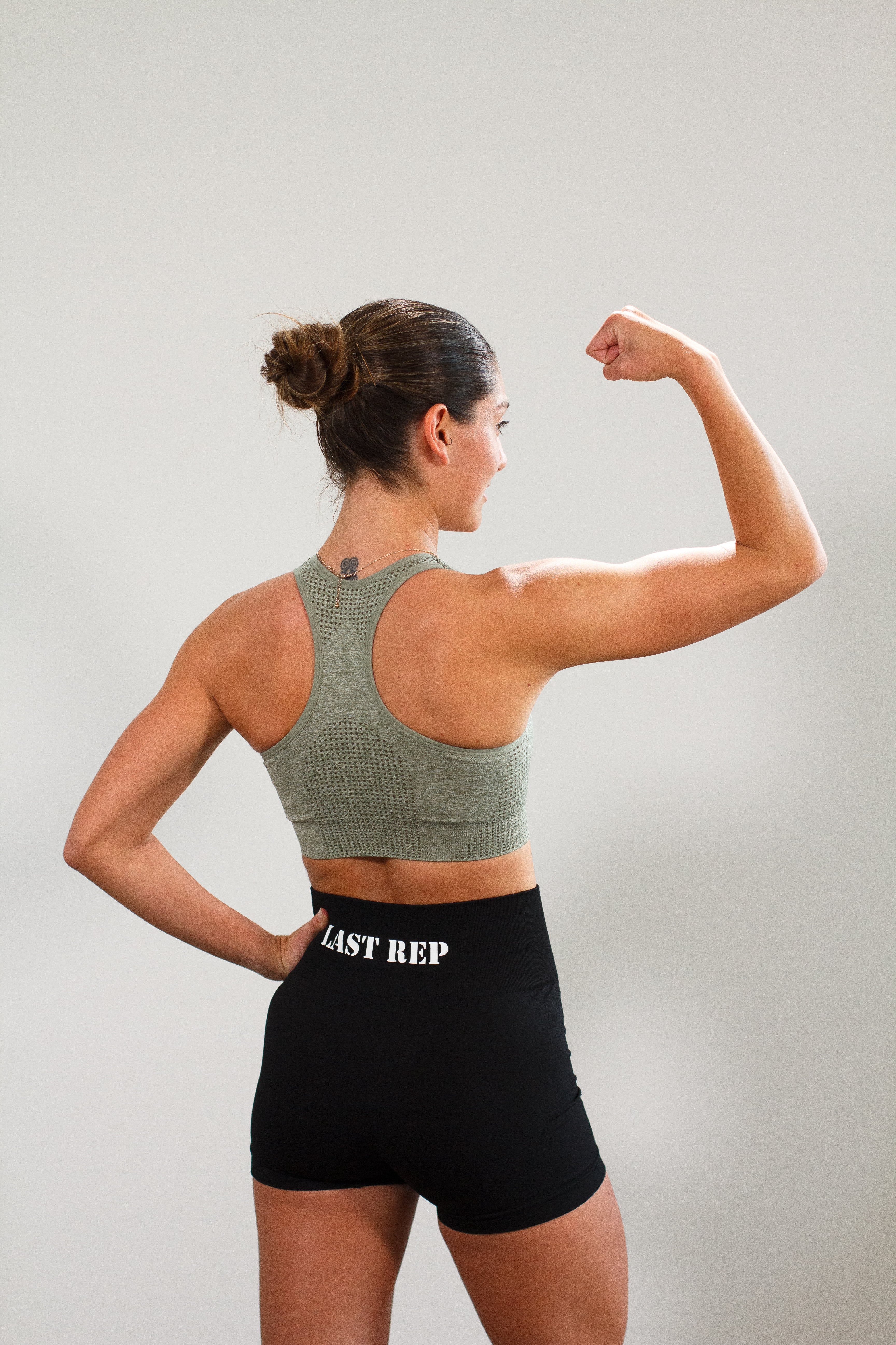 woman flexing with Last Rep green sports bra and Last Rep black biker shorts