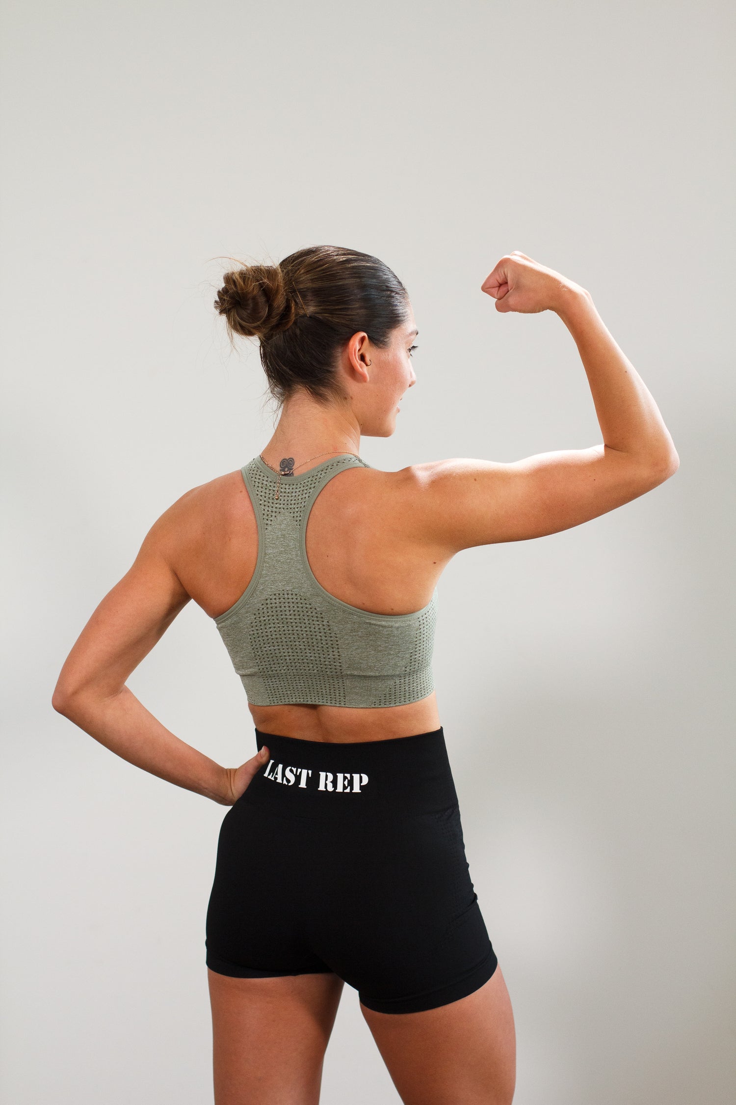 woman flexing with Last Rep green sports bra and Last Rep black biker shorts