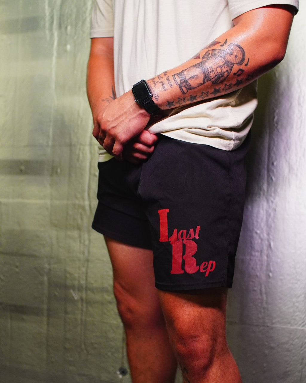 Person wearing black shorts with 'Last Rep' text, standing against a textured wall.