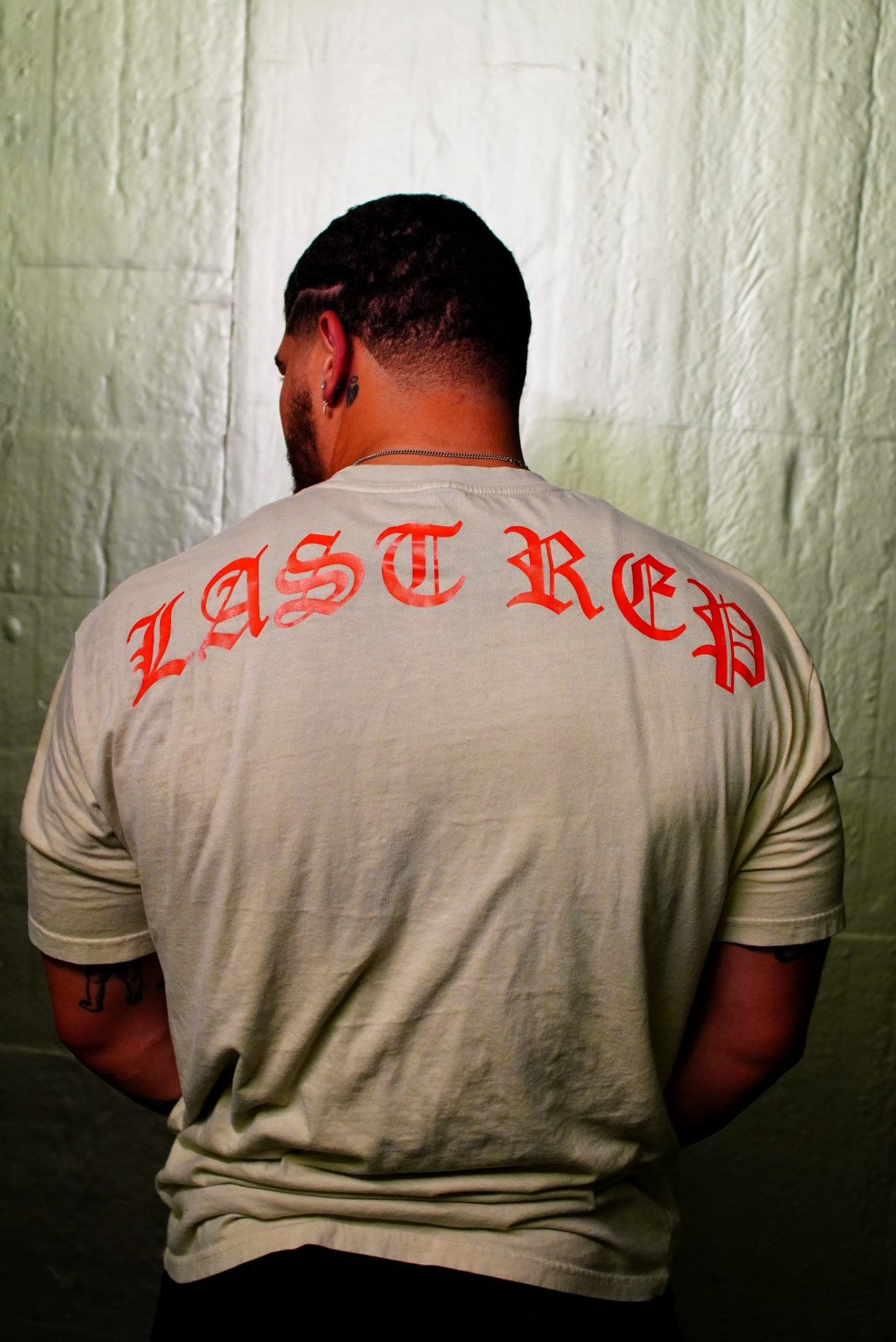 Men wearing oversized tan gym pump cover shirt, last rep across the back