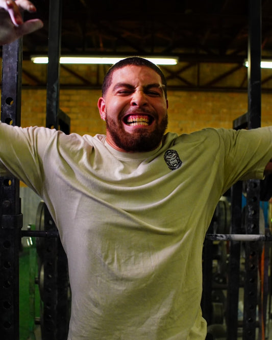 Man in a gym wearing a light green shirt with a logo, stretching his arms out.