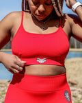 Person wearing a red sports bra and leggings with visible branding outdoors.