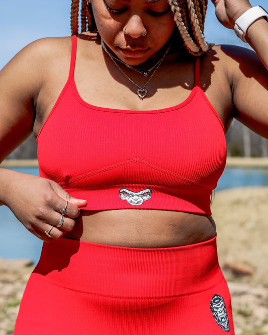 Person wearing a red sports bra and leggings with visible branding outdoors.
