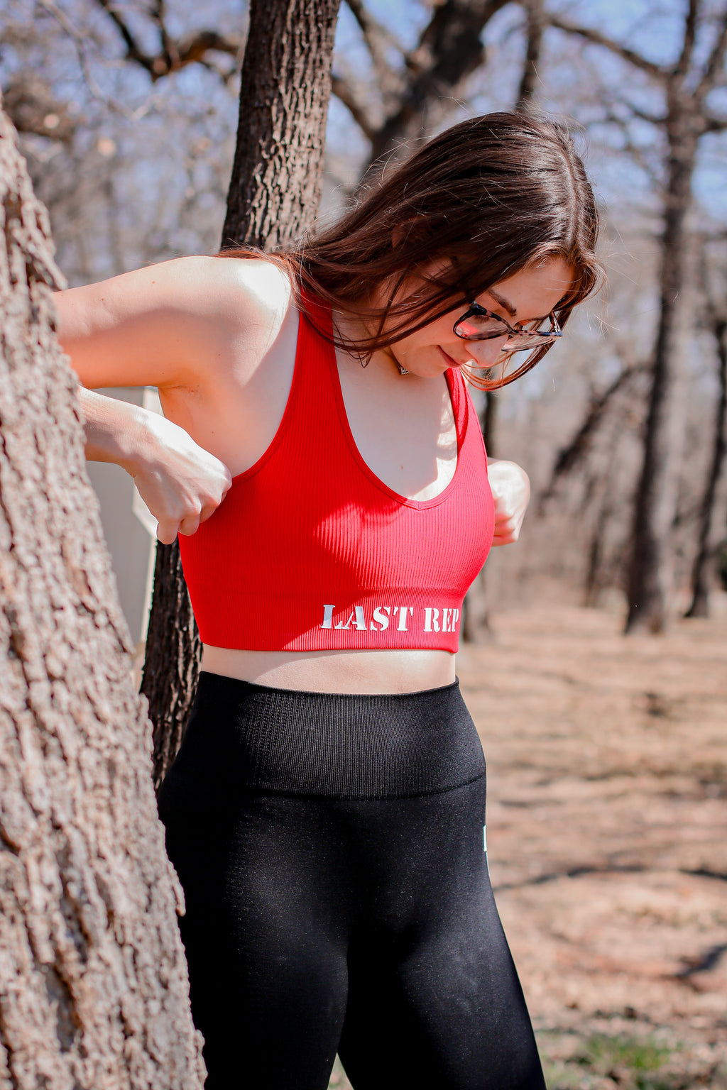 Woman posing with red Last Rep sports bra and black Last Rep leggings
